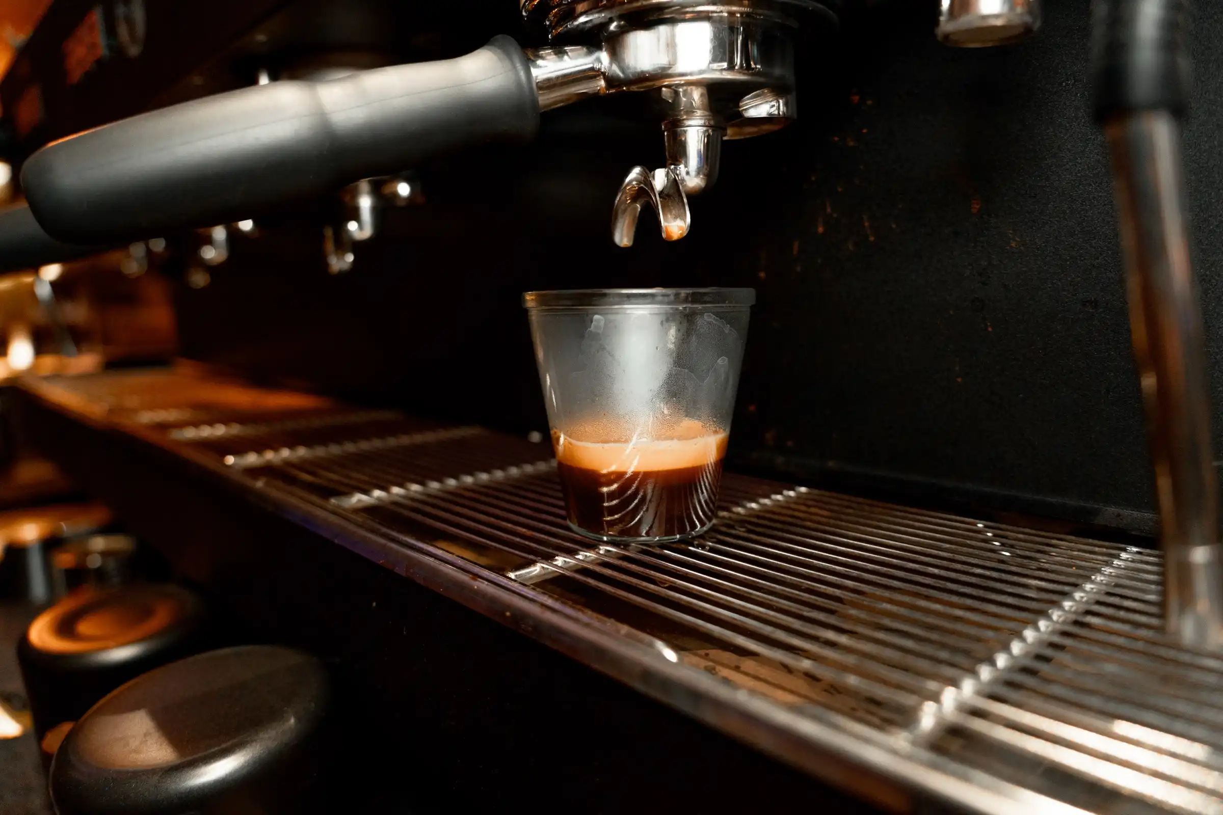 An espresso shot pulling into a small glass under the group head of our machine.